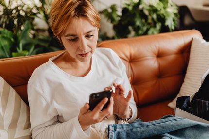 Person using a smartphone while sitting on a brown couch indoors