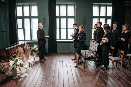 Indoor wedding ceremony with officiant, couple, and guests in a dark wood room