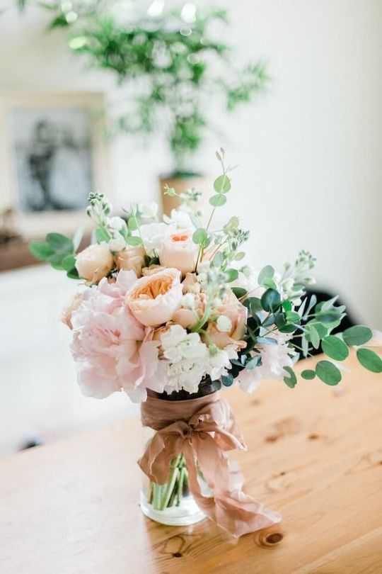Pastel bouquet with blush flowers and greenery tied with a brown ribbon on a wooden table