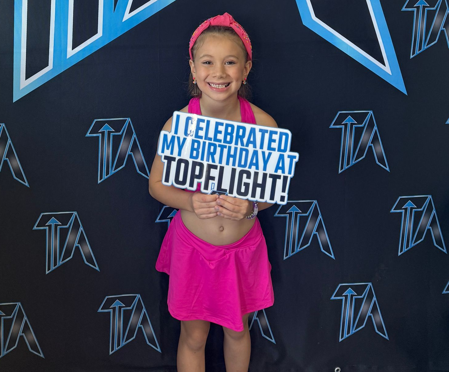 A smiling person in pink athletic wear holds a sign that reads,