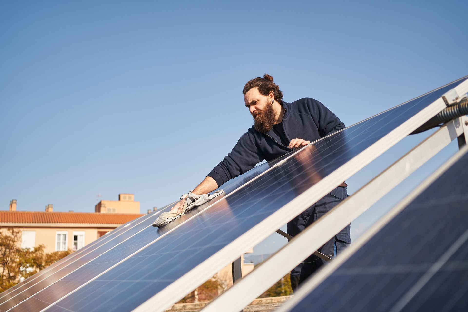 A man cleans solar panels on a rooftop under a clear blue sky.