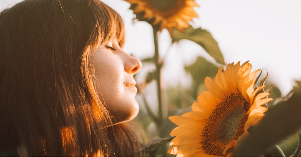 Young woman smelling a sunflower with her eyes closed and a content expression