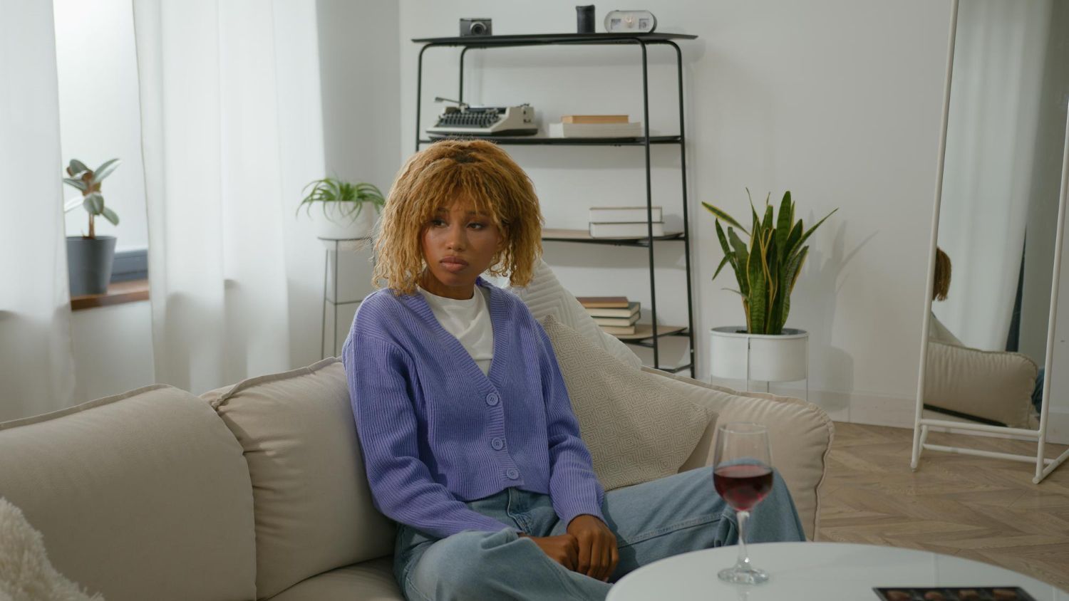 Young woman sitting calmly on a sofa in her home with a glass of wine.