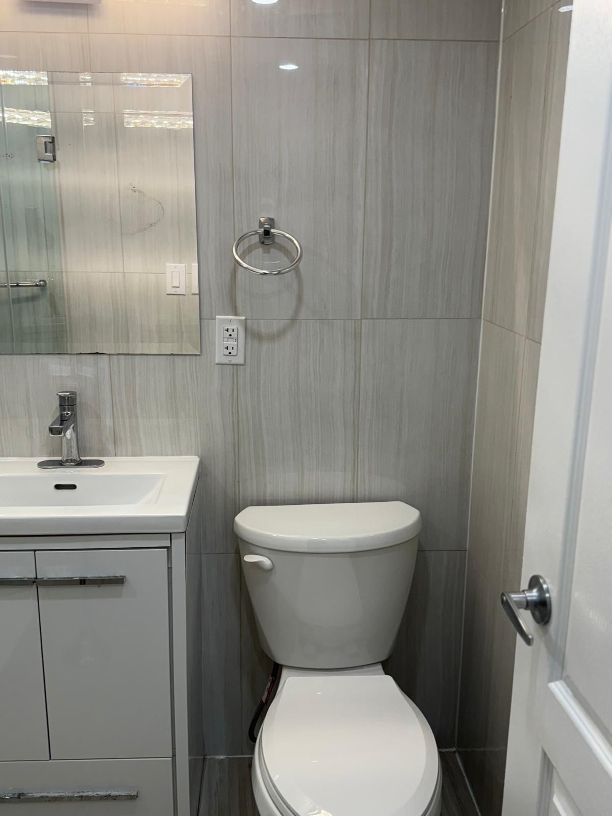 A bathroom with a toilet , sink and mirror.
