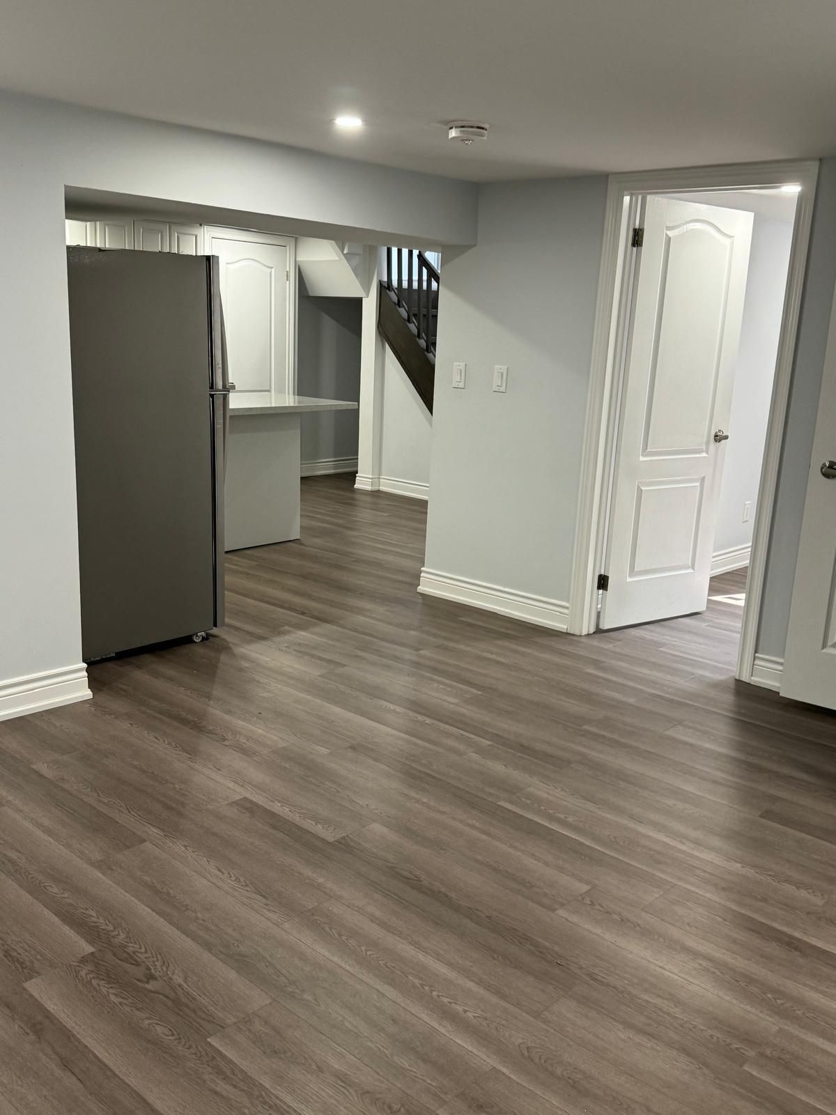 An empty basement with hardwood floors and a refrigerator.