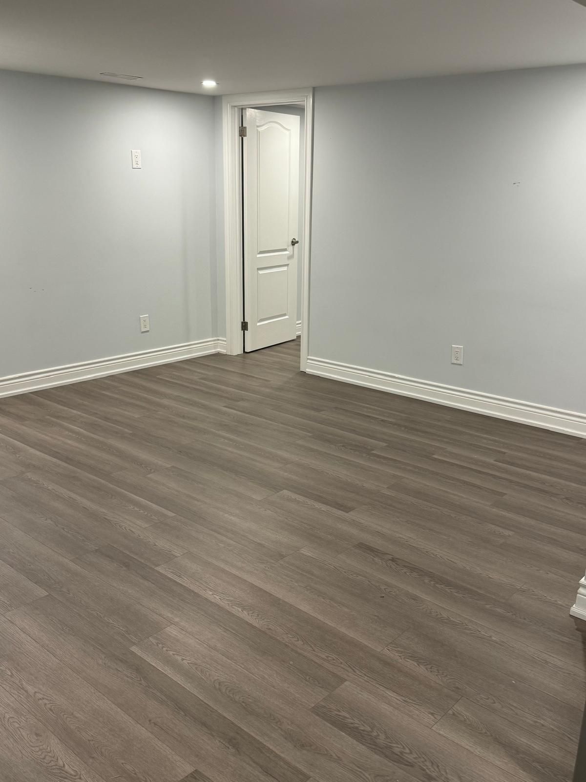 An empty basement with hardwood floors and white walls.