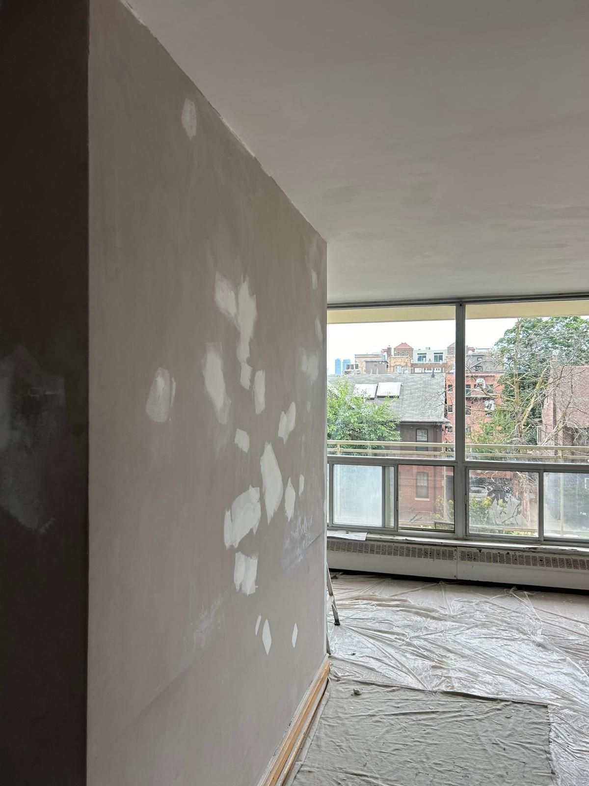 A room with a large window and a wall that is being plastered.
