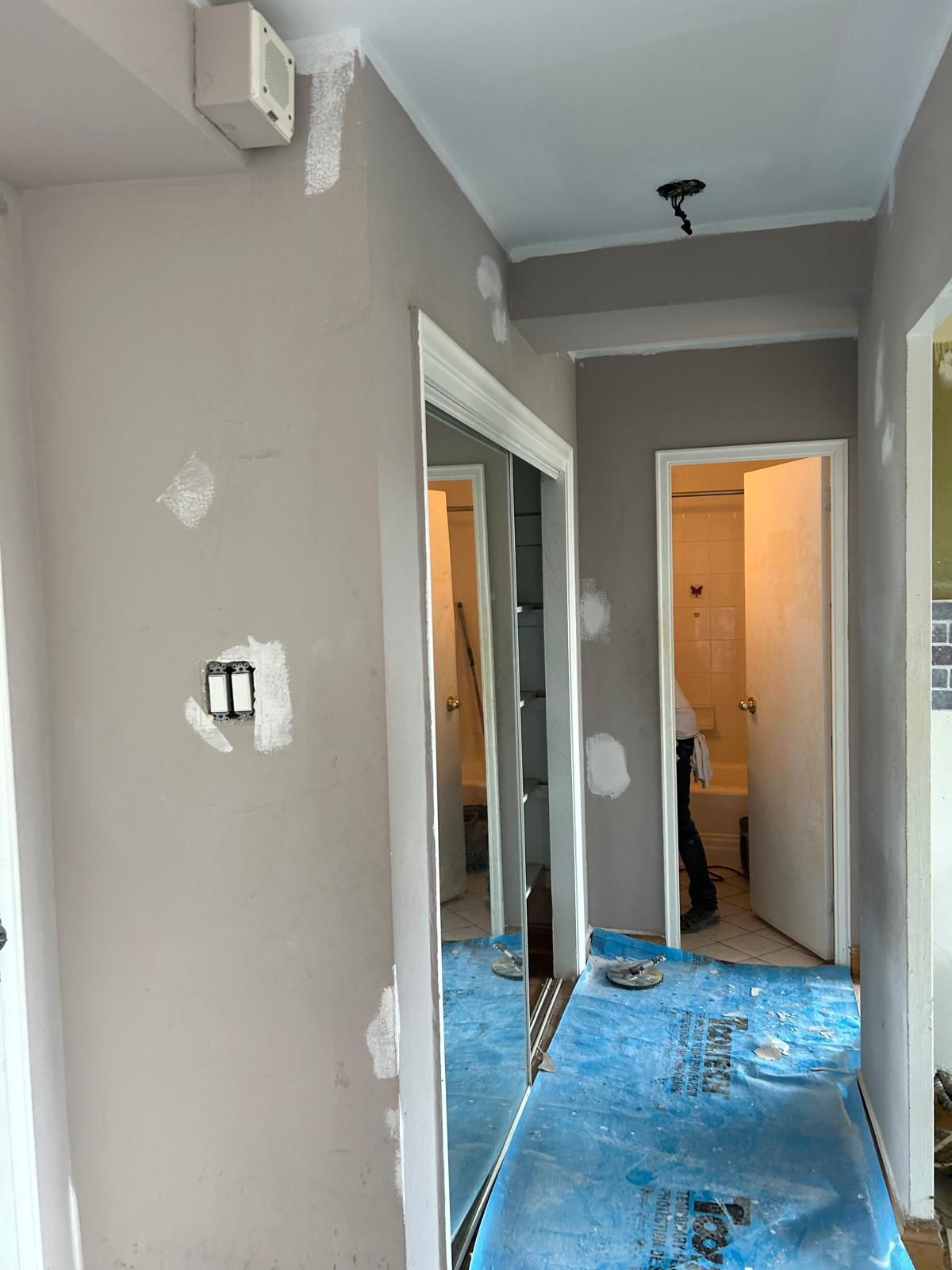 A hallway with a blue tarp on the floor and a mirror on the wall.