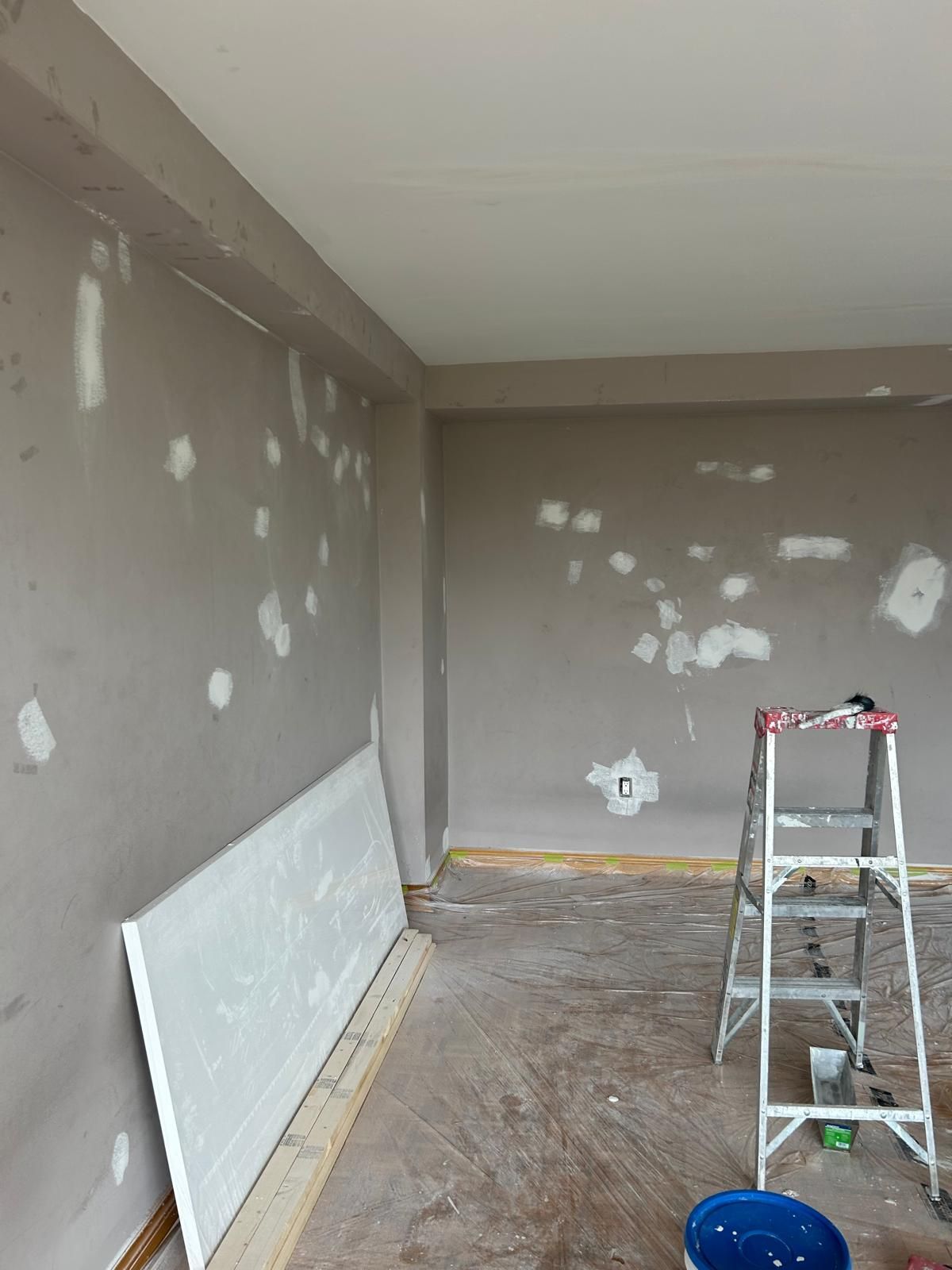 A room with a ladder and a bucket of paint on the floor.