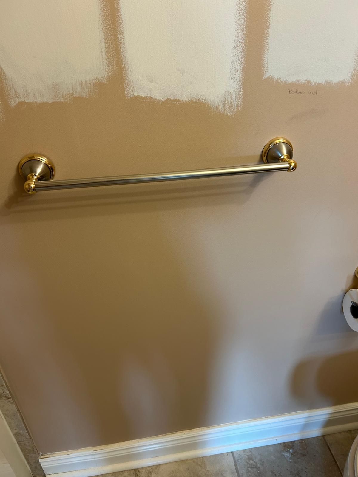 A towel rack is hanging on a wall in a bathroom next to a toilet paper dispenser.