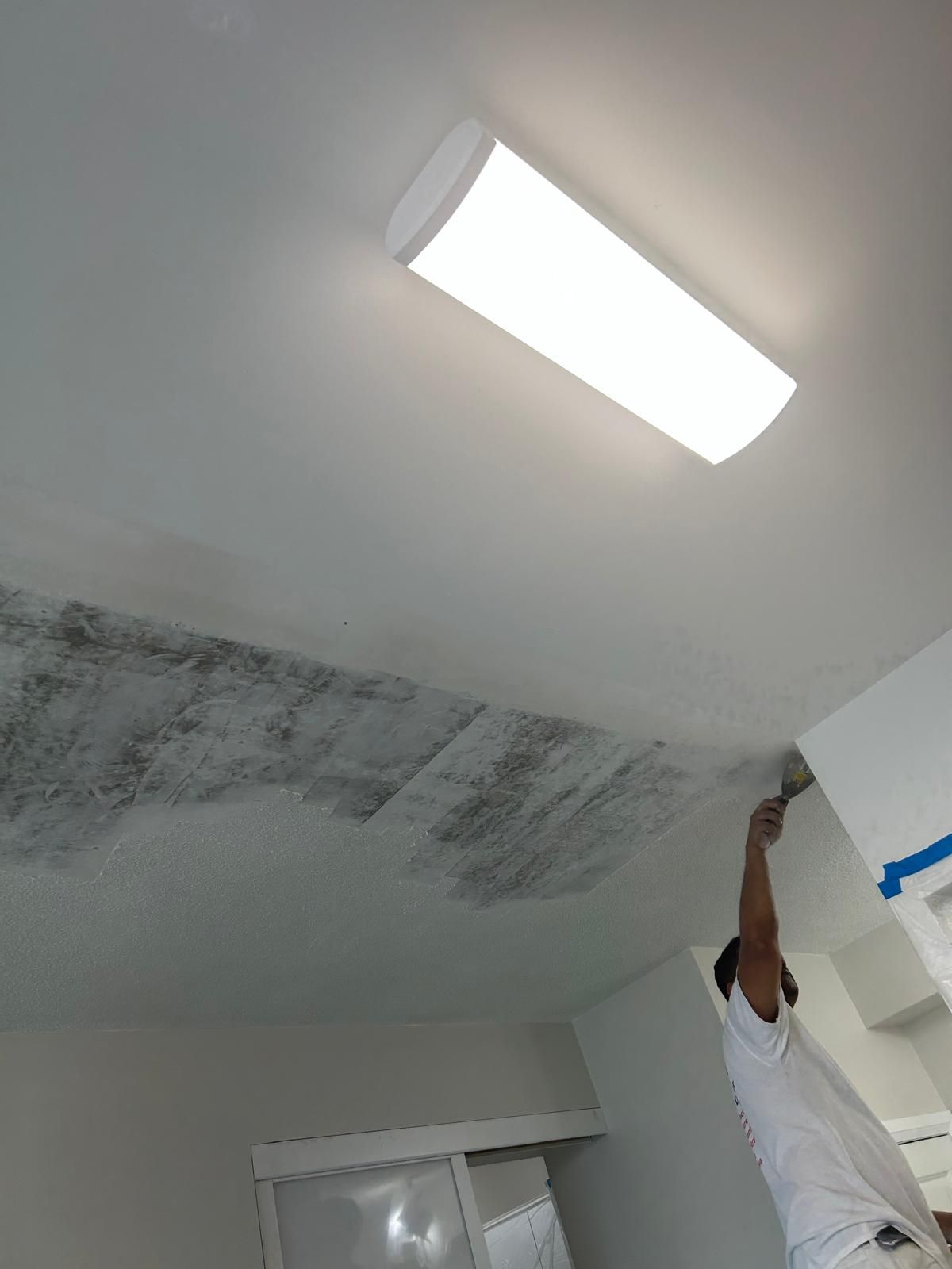 A man is painting the ceiling of a room with a brush.
