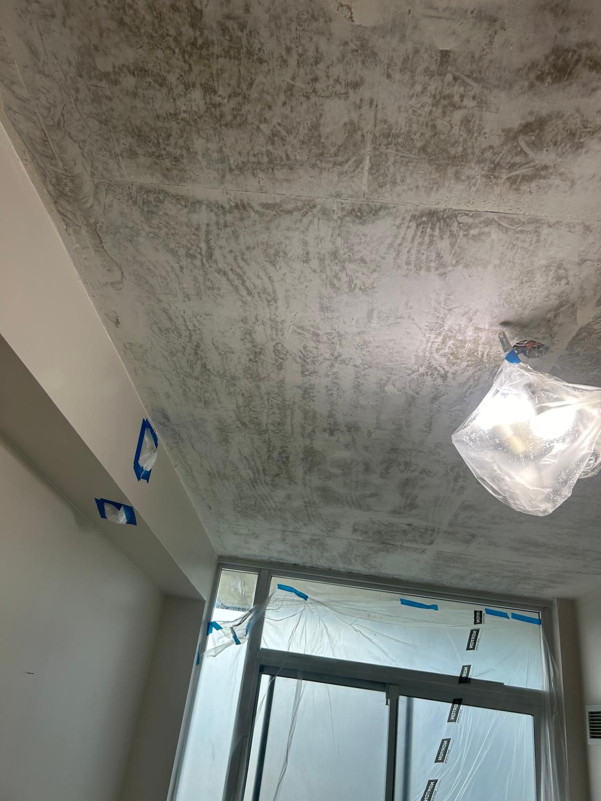 A room with a ceiling that is being painted and a window.