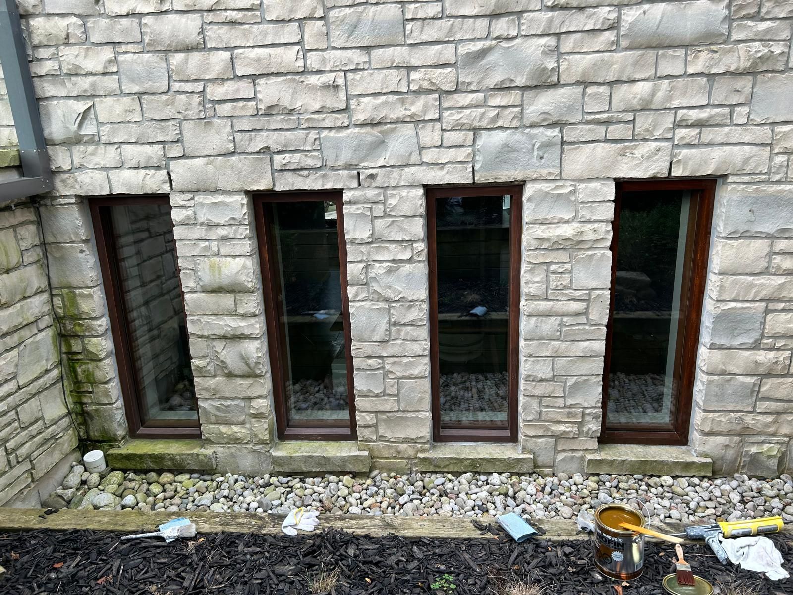 A brick building with three windows and a bucket of paint on the ground.