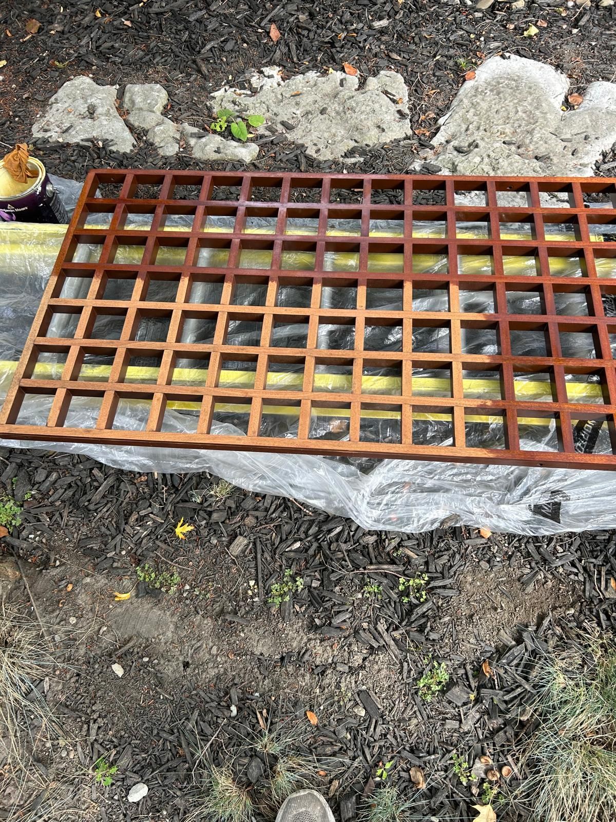 A wooden trellis is sitting on top of a plastic bag on the ground.