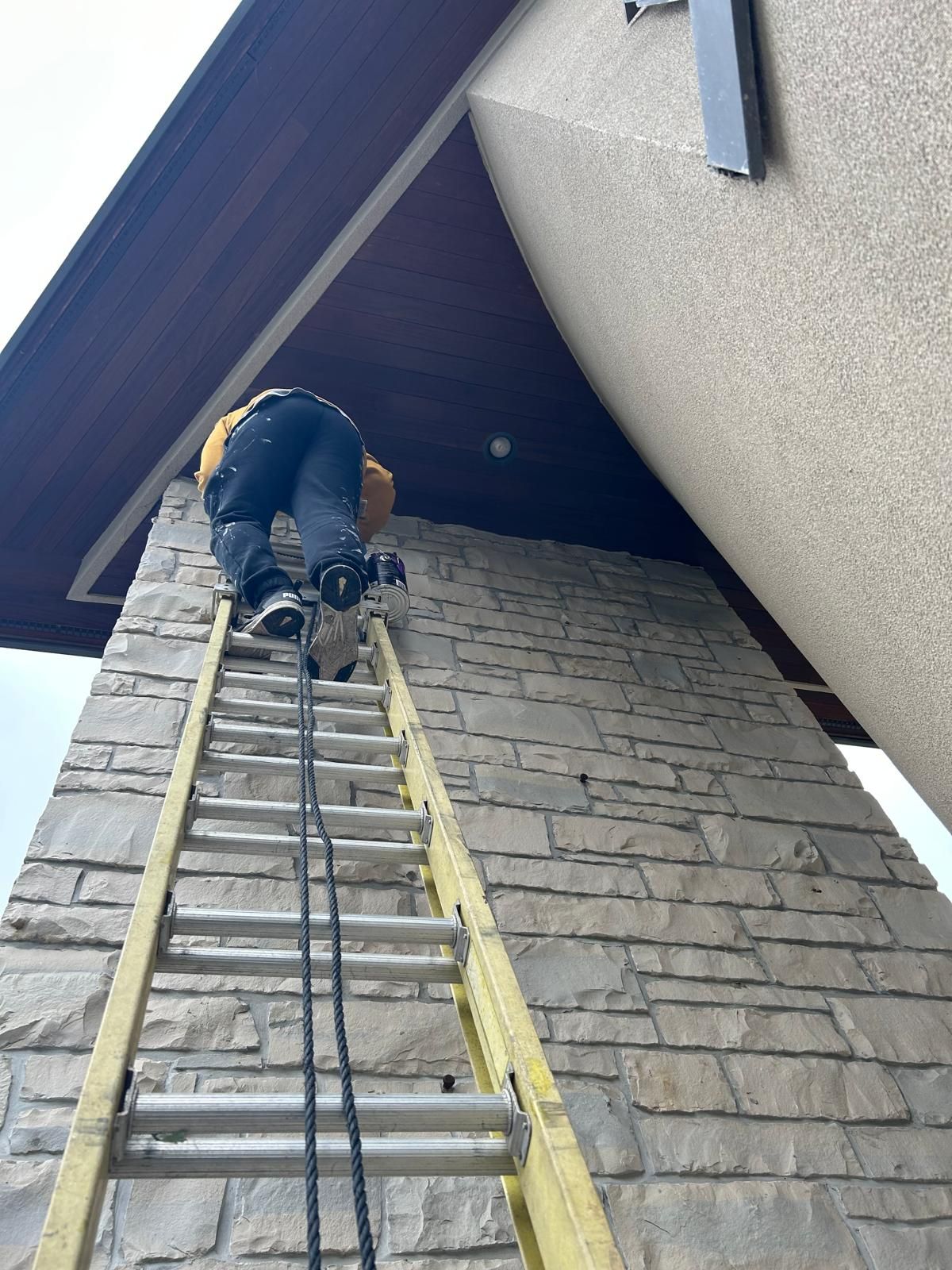 A man is climbing up a ladder on a brick wall.