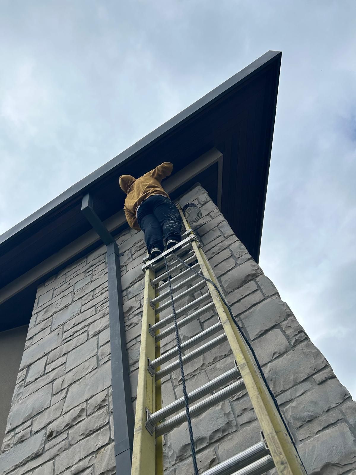 A man is climbing up a ladder on top of a brick building.