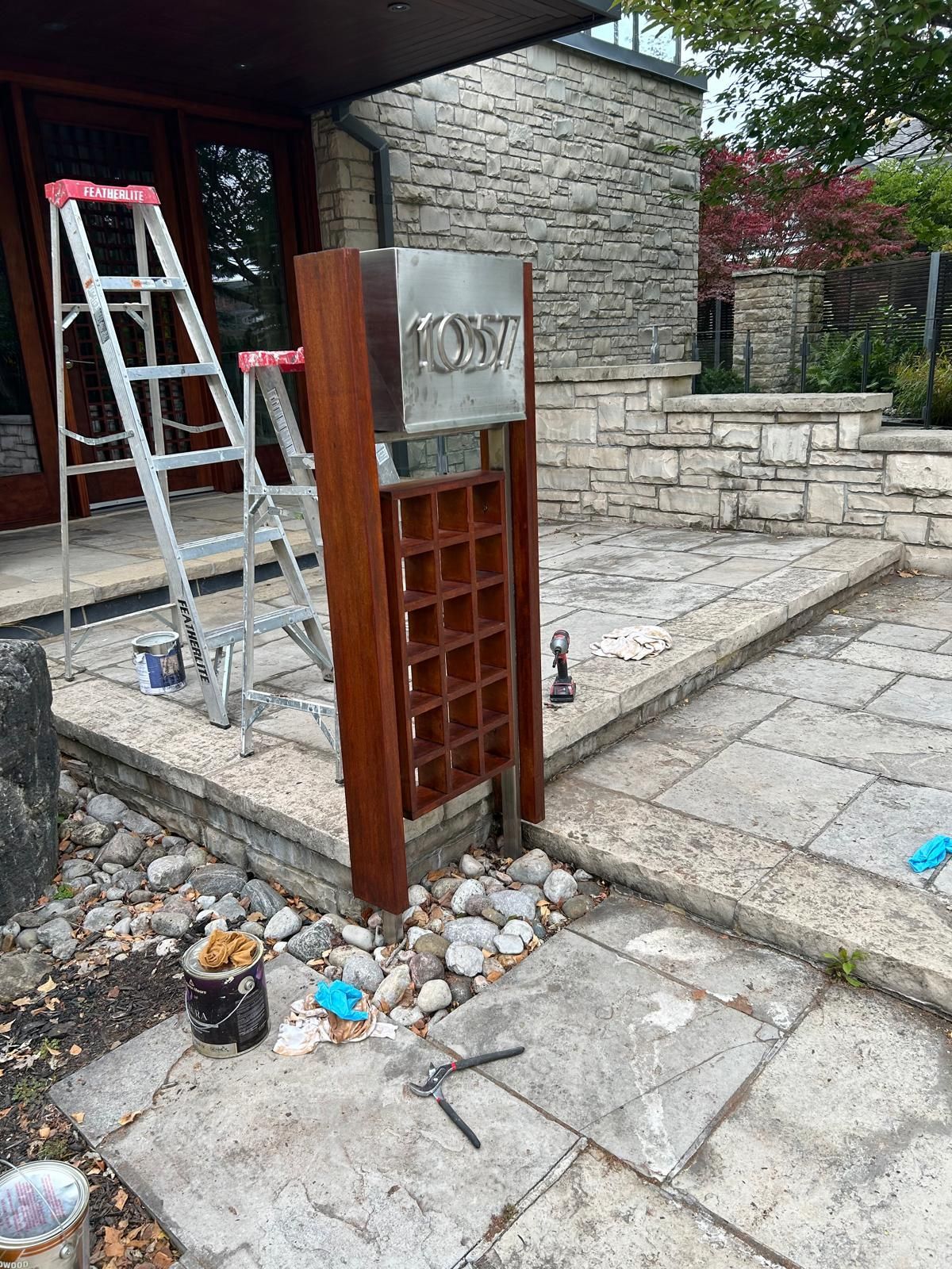 A wooden mailbox is being painted in front of a stone building.