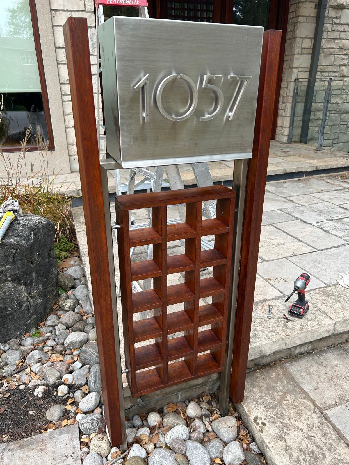 A stainless steel mailbox is sitting on a wooden post in front of a building.