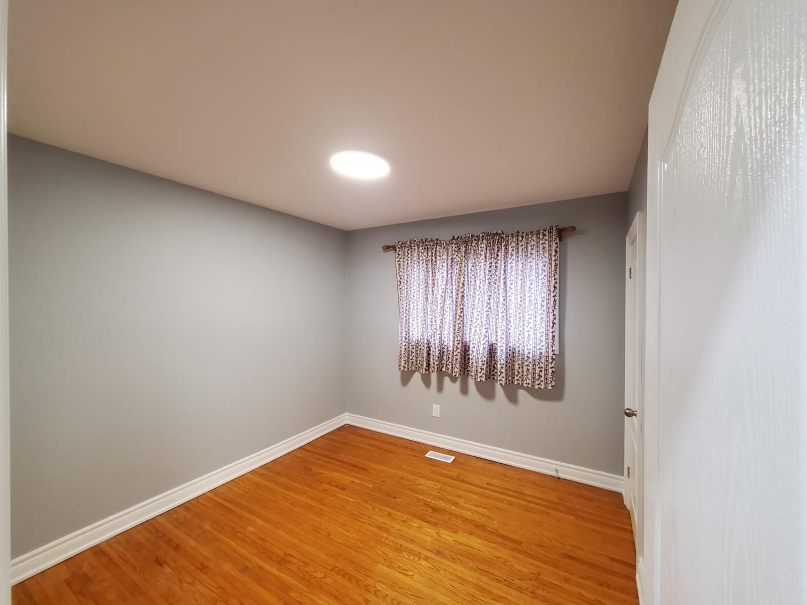 An empty bedroom with hardwood floors and a window.