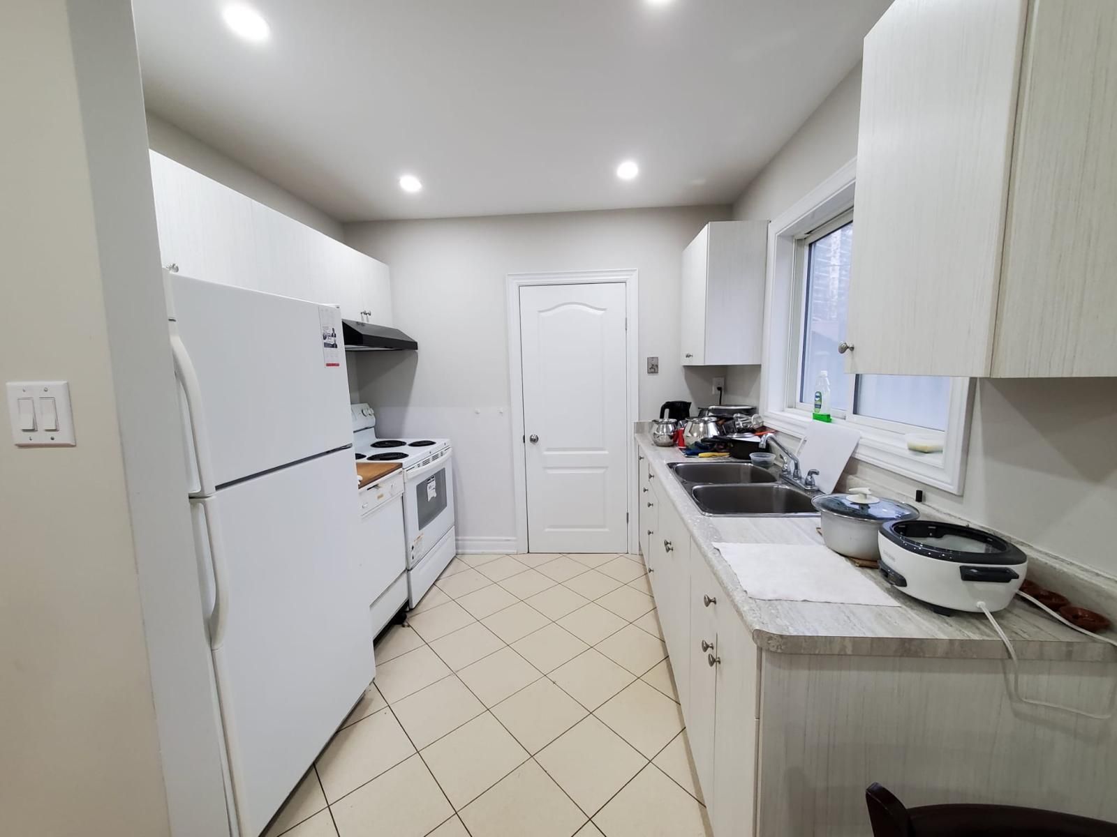 A kitchen with white cabinets , a refrigerator , a stove , a sink , and a window.