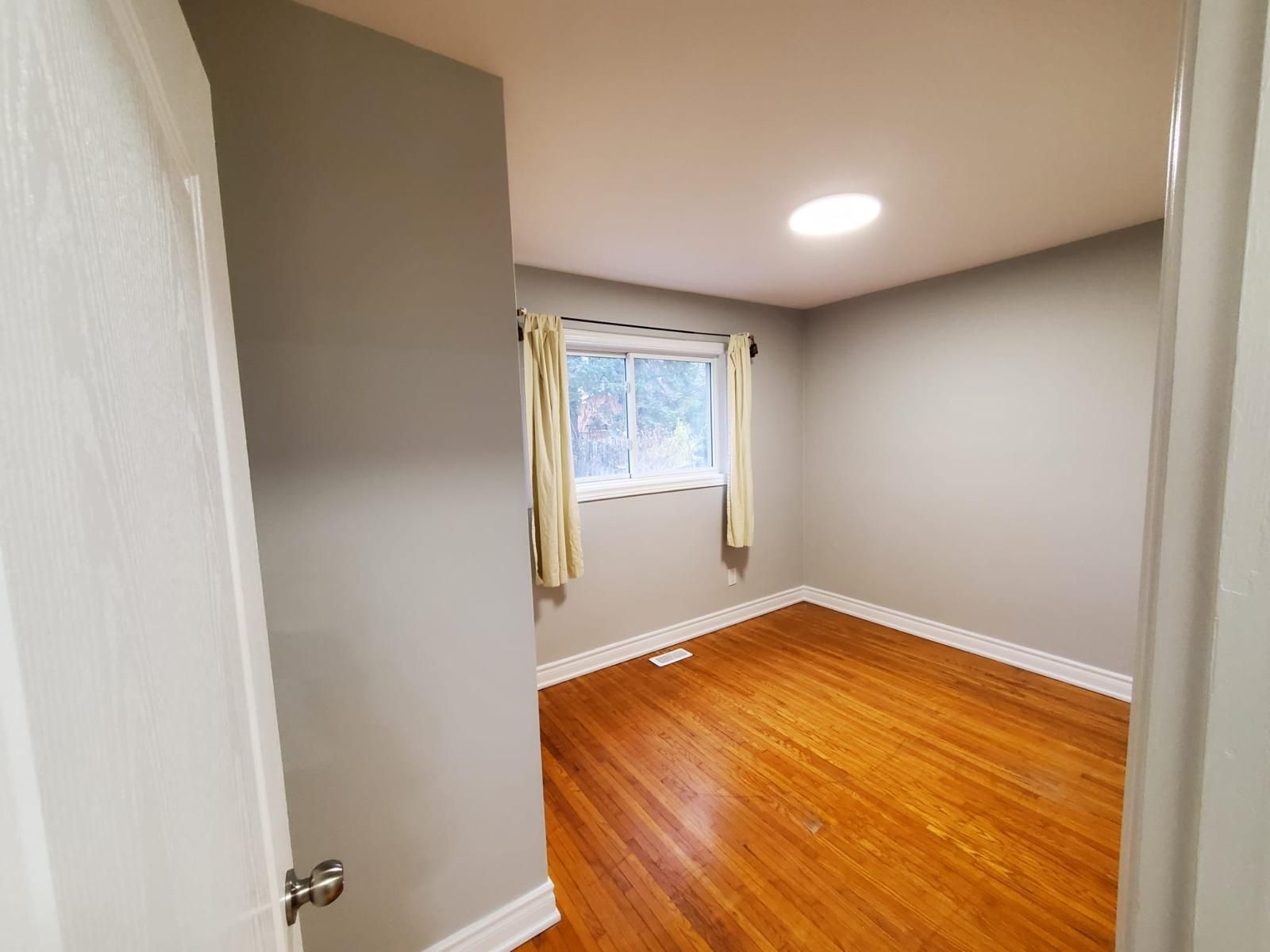 An empty bedroom with hardwood floors and a window.