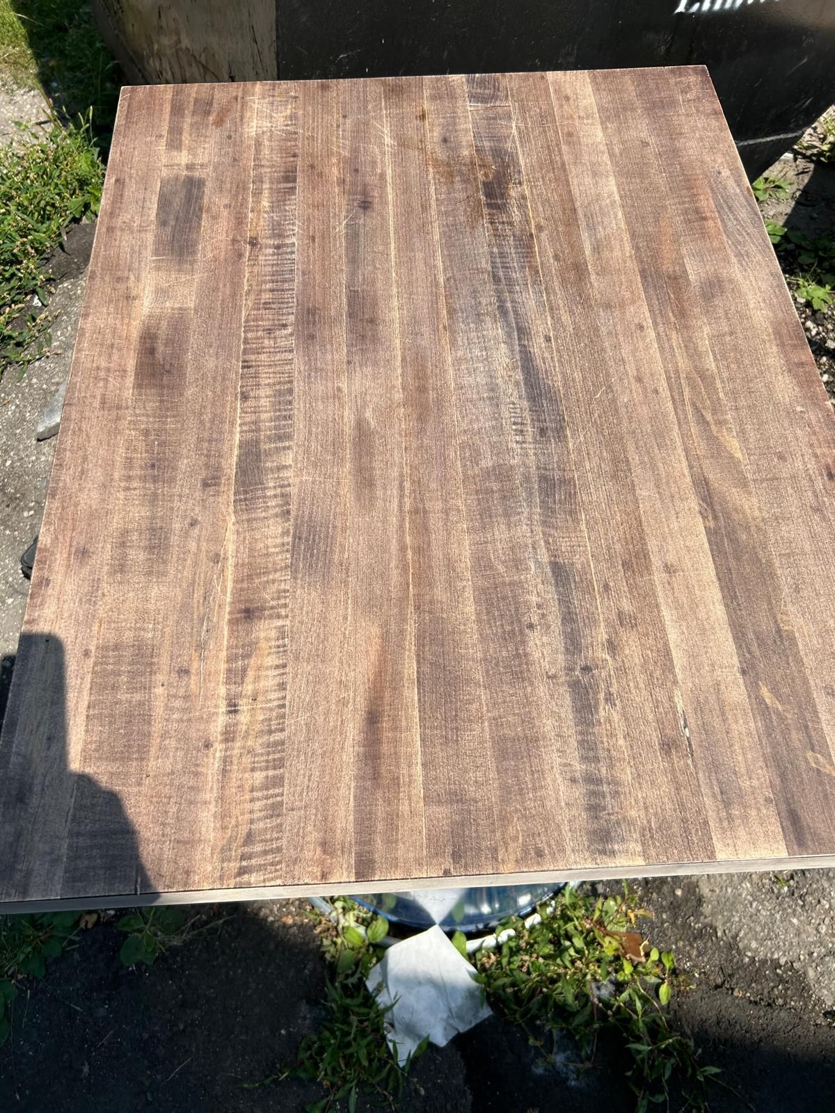 A wooden table with a metal base is sitting on the ground.