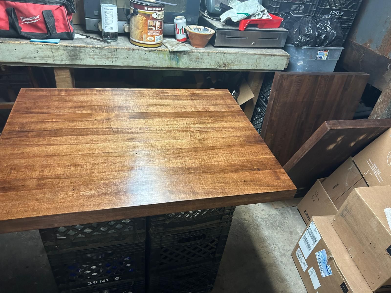 A wooden table is sitting in a room surrounded by boxes.