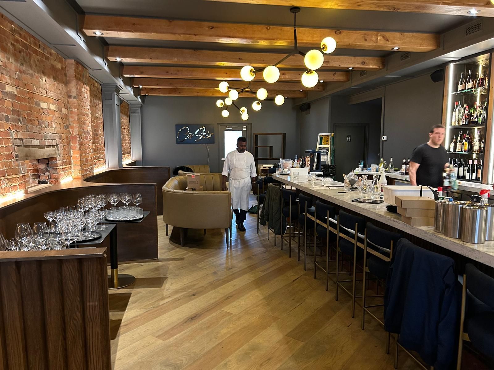 A man in a white coat is standing in a restaurant with a long bar.