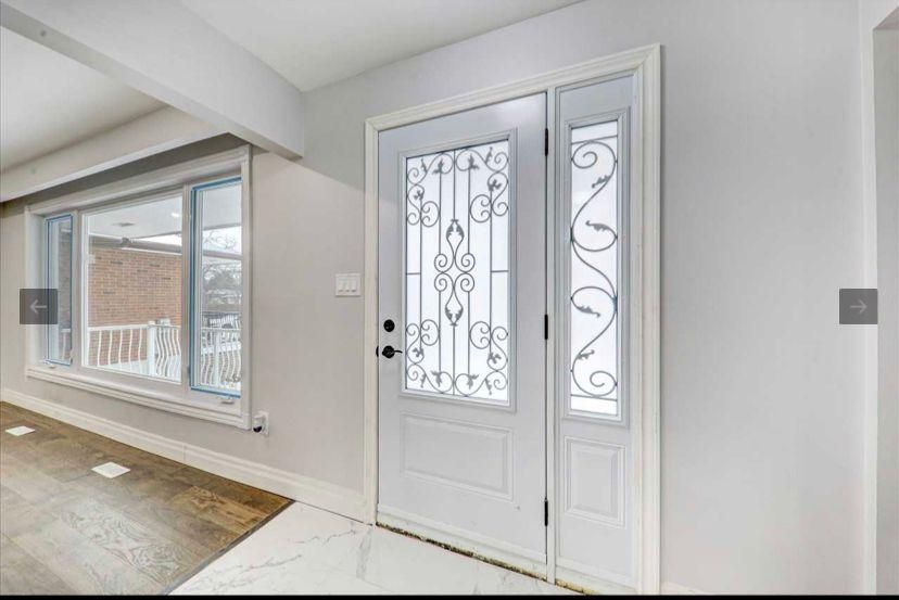 A white door with a wrought iron design is in a hallway next to a window.