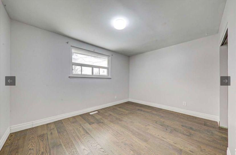 An empty bedroom with hardwood floors and a window.