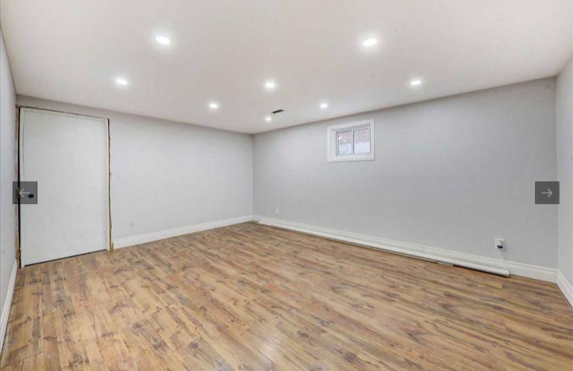 An empty basement with hardwood floors and a window.
