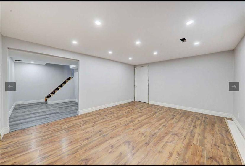An empty basement with hardwood floors and white walls.