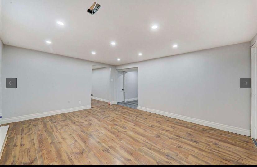 An empty basement with hardwood floors and white walls.