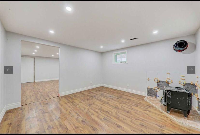 An empty basement with hardwood floors and a wood stove.