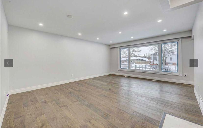An empty living room with hardwood floors and a large window.