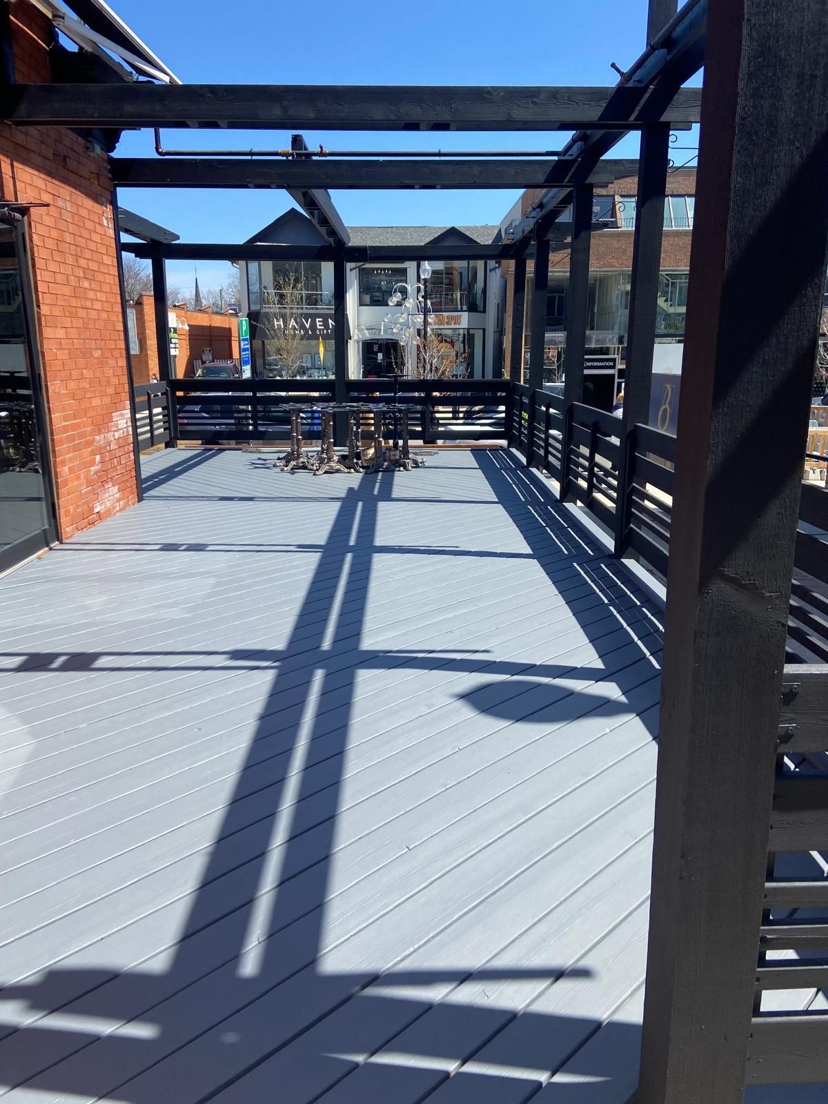 A deck with a pergola and a brick building in the background