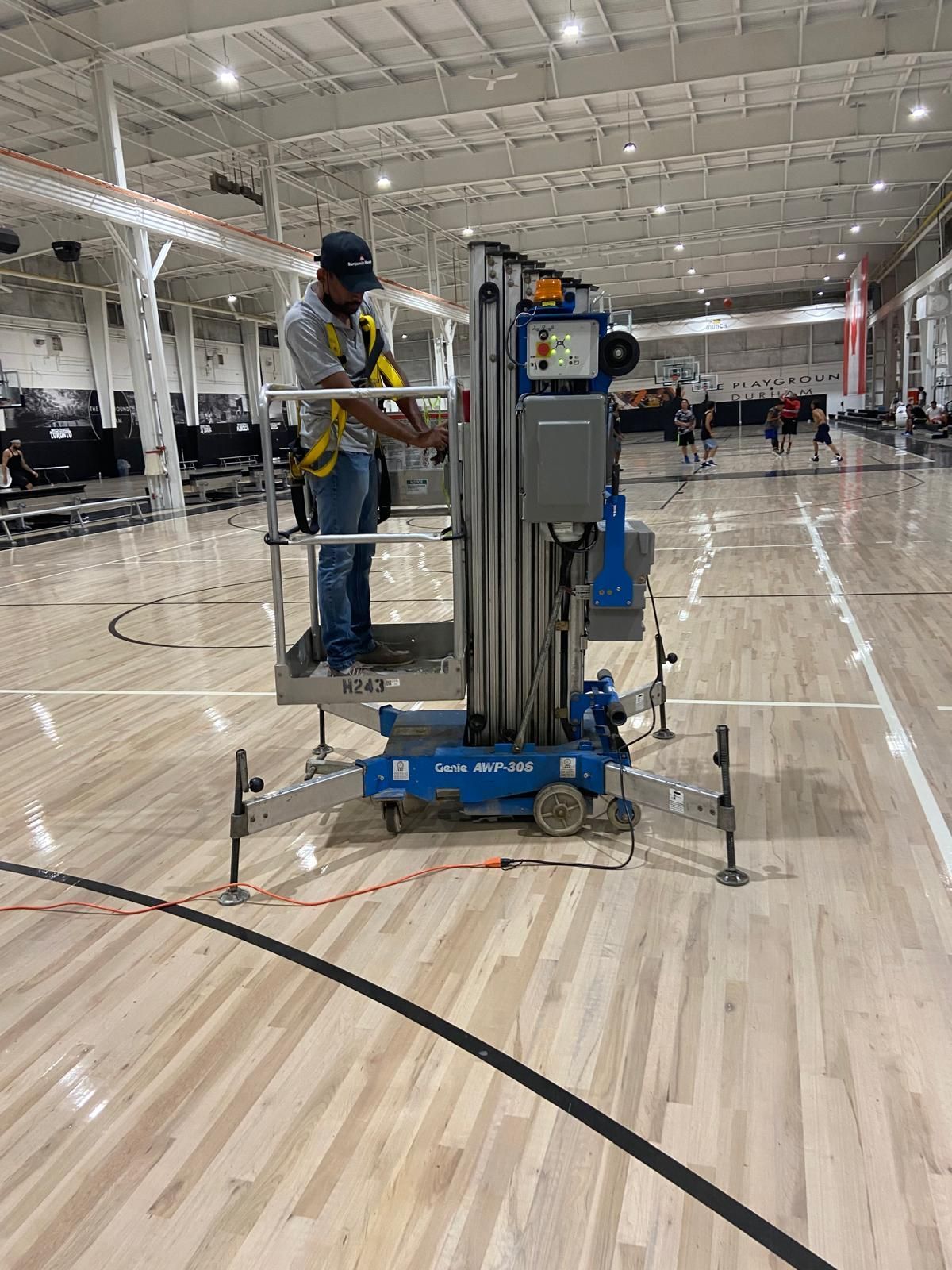 A man is standing on a lift on a basketball court.