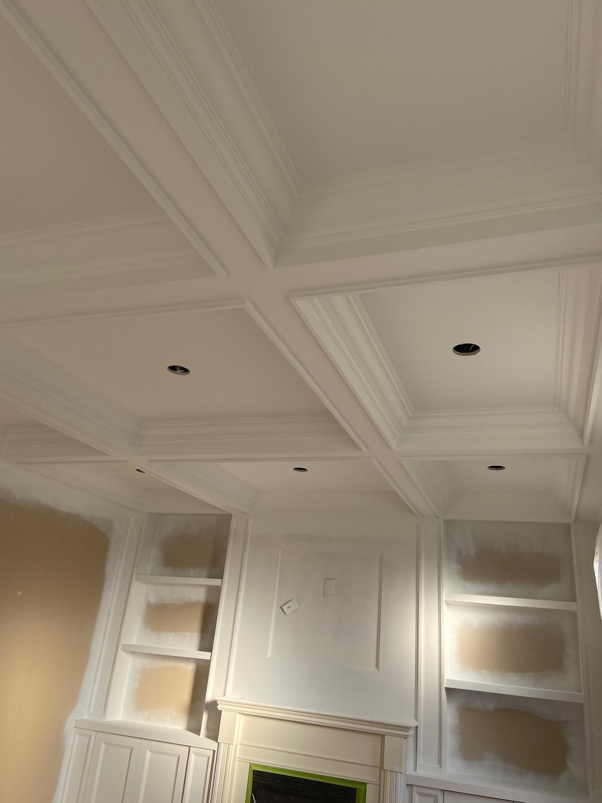 A living room with a fireplace , shelves , and a coffered ceiling.