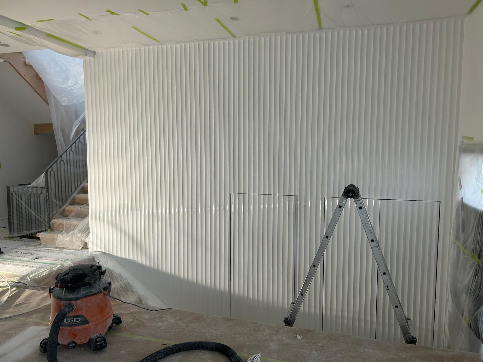 A room with a ladder and a vacuum cleaner in front of a wall.