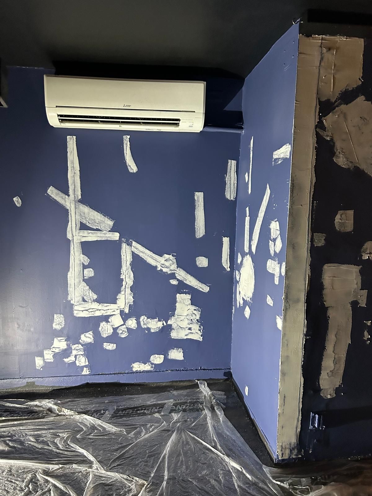 A room with a blue wall and a white air conditioner on the ceiling.