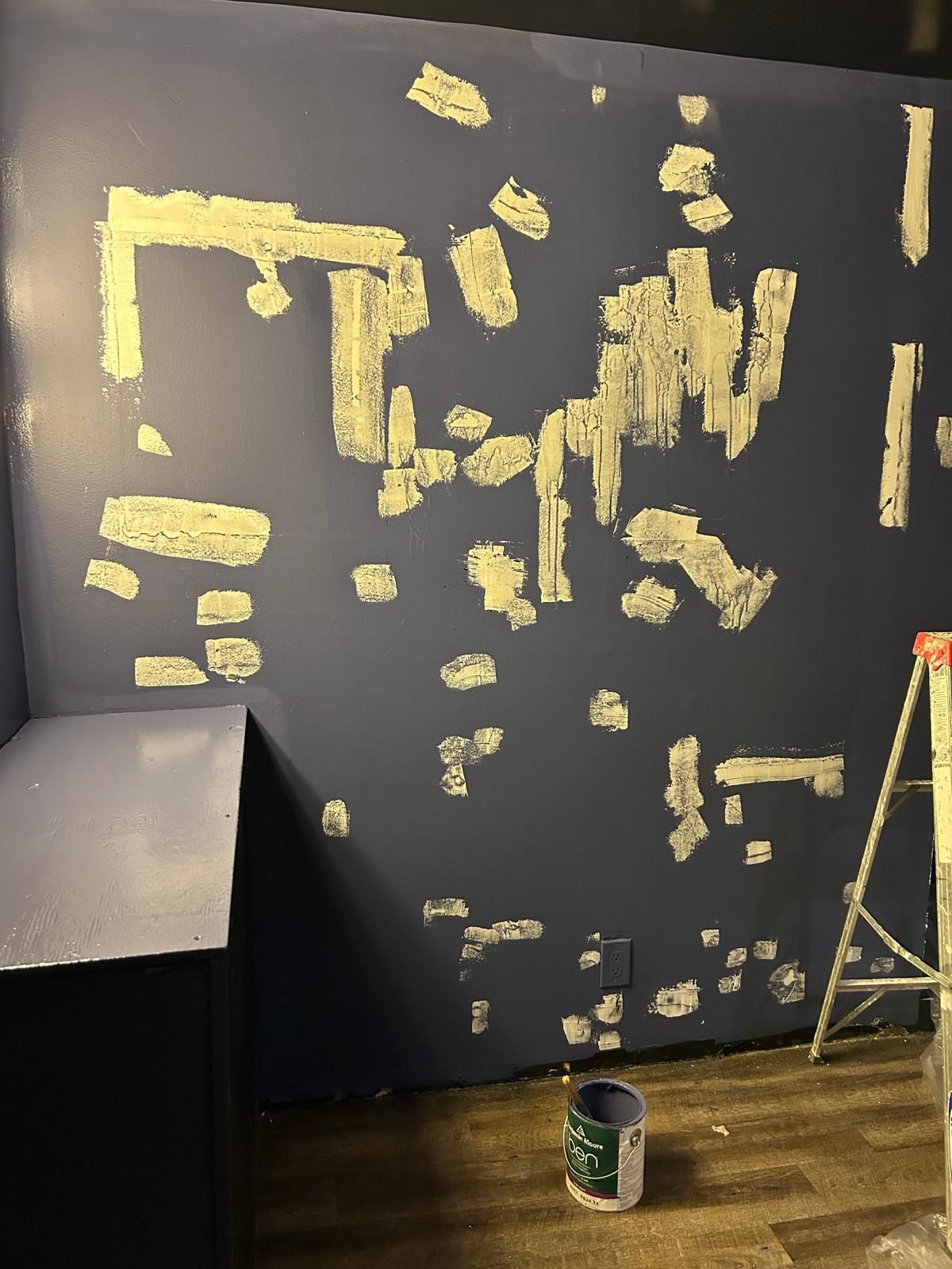 A blue wall with a ladder and a bottle of paint