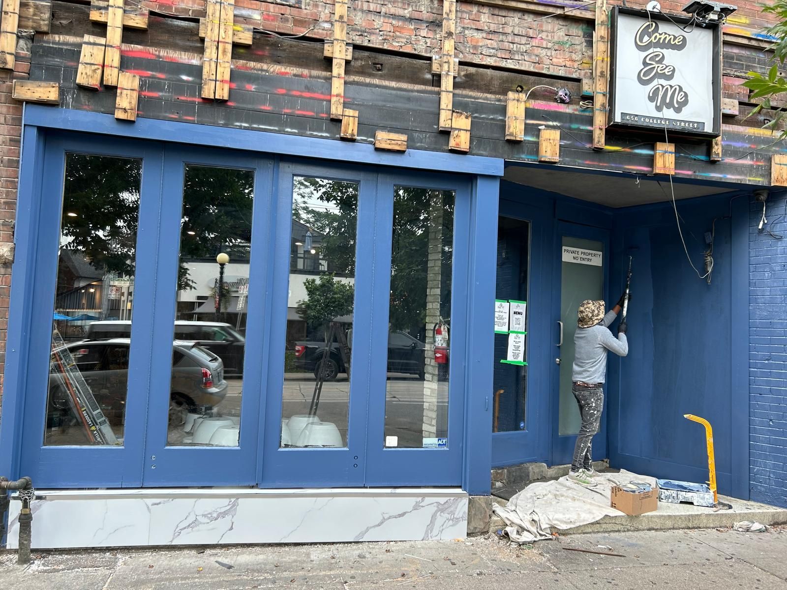 A woman is standing in front of a blue building.