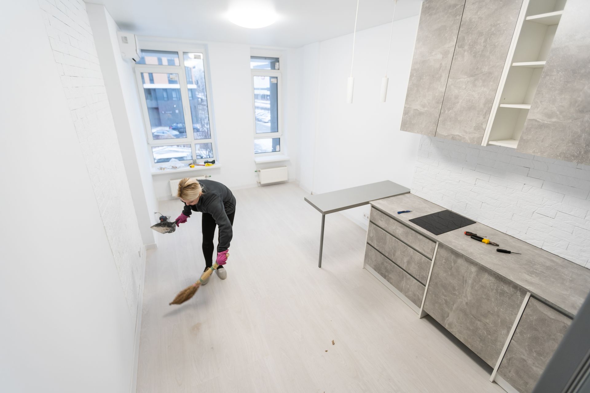 A woman is sweeping the floor of a kitchen with a broom.