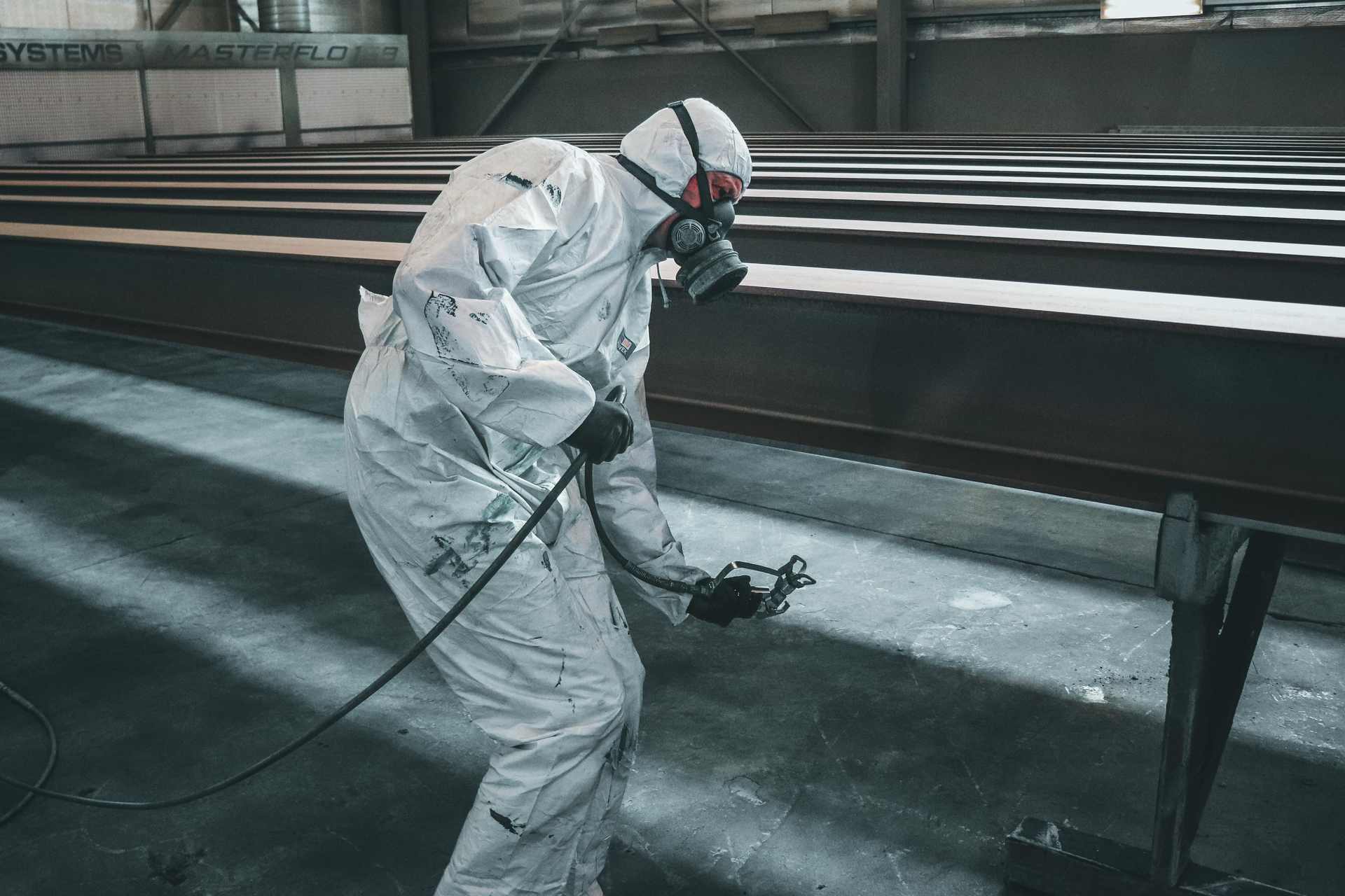 A man in a protective suit is spray painting a metal structure.