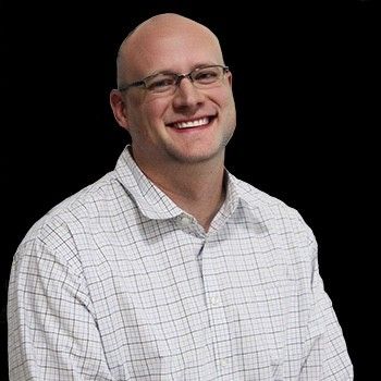 Smiling bald man in glasses wearing a white checkered shirt against a black background