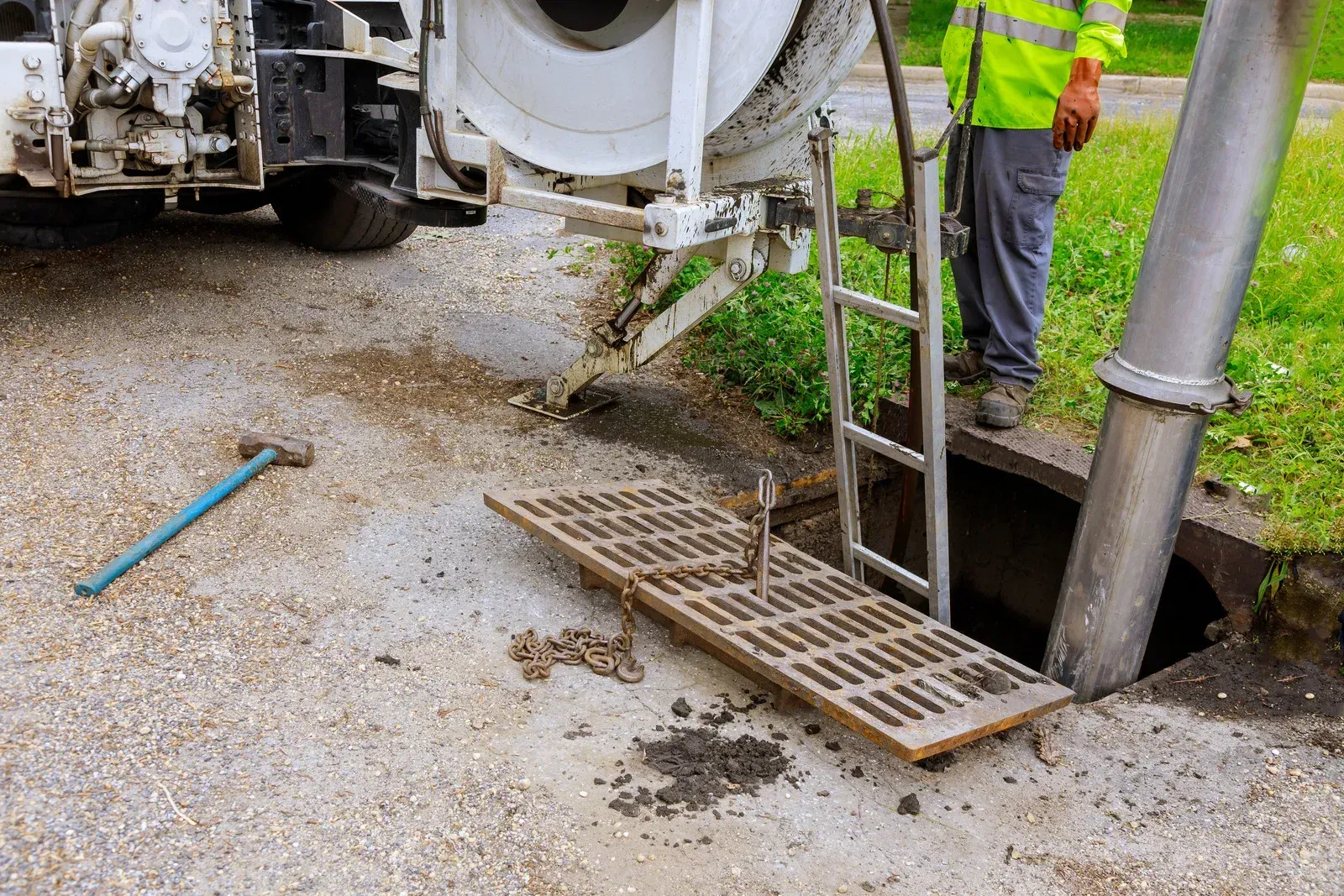 Sewer drain cleaning; worker in safety vest, using truck-mounted equipment to vacuum debris from a manhole.
