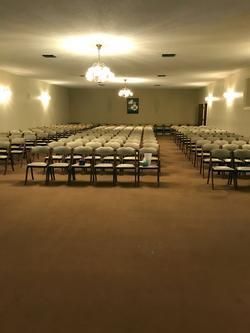 Empty banquet hall with rows of chairs facing a central aisle under warm ceiling lights