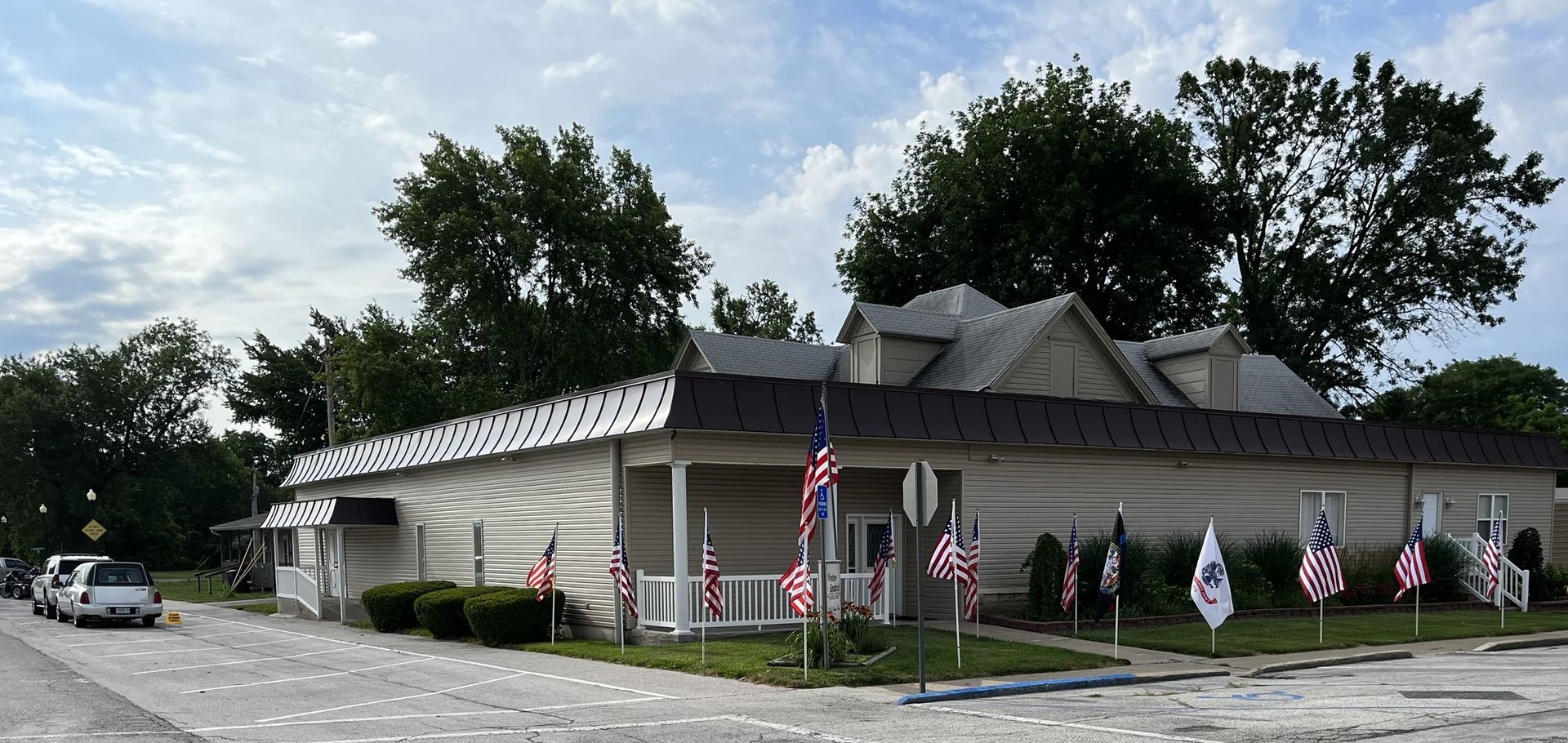Small roadside building with many American flags and a parked car under cloudy skies.