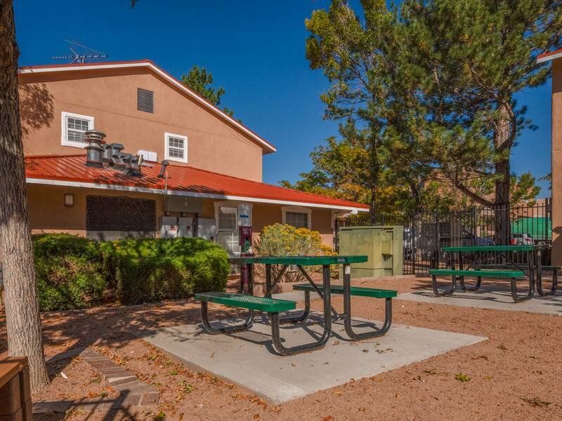 Outdoor communal area with green picnic tables and a tan building at Santa Fe Suites in Santa Fe, NM.