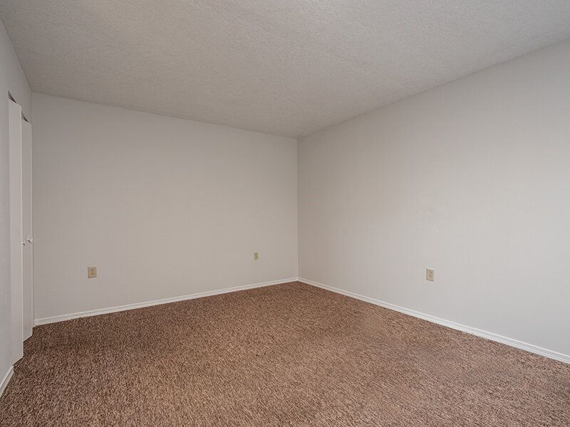 Empty beige-carpeted room with white walls and electrical outlets at Santa Fe Suites in Santa Fe, NM.